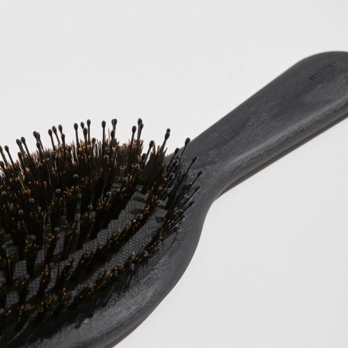 Eine schwarze Haarbürste mit Griff und dicht stehenden Borsten. Der Hintergrund ist einfach und hell.