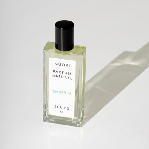Eine klare Parfümflasche mit schwarzem Deckel und weißem Etikett, die auf der Oberfläche ein Schatten wirft.