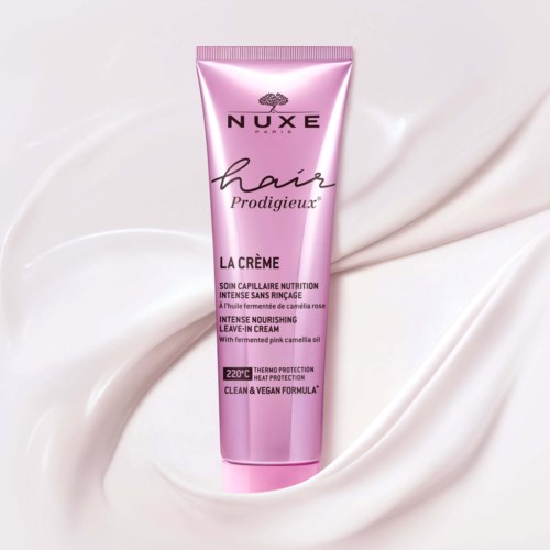 Pink tube of Nuxe hair nourishing cream with rose scent on soft white fabric background.