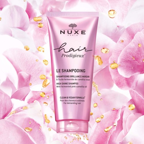 Pink shampoo bottle with gold and flower petals background, labeled 'Nuxe Hair Prodigieux' and 'High Shine Shampoo'.