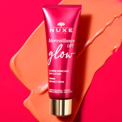 Pinkfarbene Tube mit Nuxe Glow Radiance Creme auf pinkem und pfirsichfarbenem Hintergrund. Beschriftung erwähnt Lift- und Strahlungseffekte.