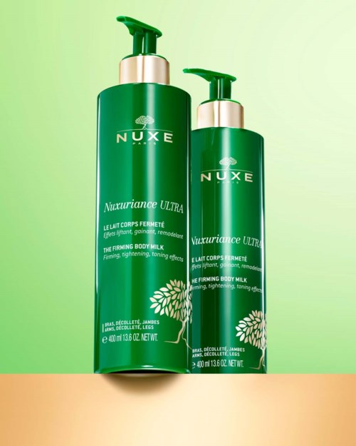 Två gröna flaskor med Nuxe body milk med pump på en grön bakgrund.
