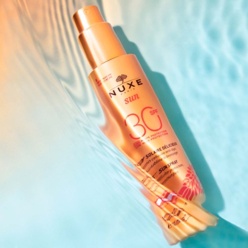 En solskyddsflaska märkt 'NUXE Sun SPF 30' på en färgglad, abstrakt bakgrund med blå och orange nyanser.