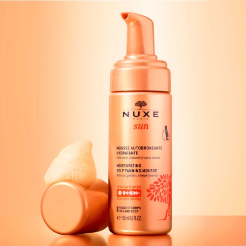 A bottle of Nuxe Sun moisturizing self-tanning mousse with an orange pump, next to a foam applicator.
