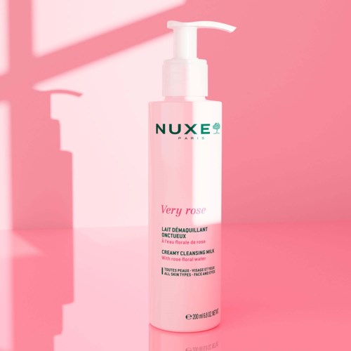 A pink bottle with a pump, labeled 'Very Rose' by Nuxe, stands on a pink background.