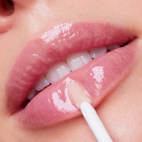 A close-up of lips with glossy pink lipstick and a cotton swab touching the lip area.
