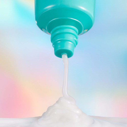 A tube with white cream or soap pouring out on a colorful, cloudy background.