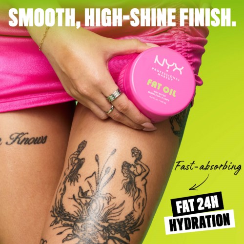 A woman with tattoos holds a pink jar of NYX Fat Oil on her thigh, advertising smooth, shiny, and hydrated skin.