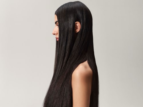 A woman with long, straight, black hair, looking to the side, with a plain light background.