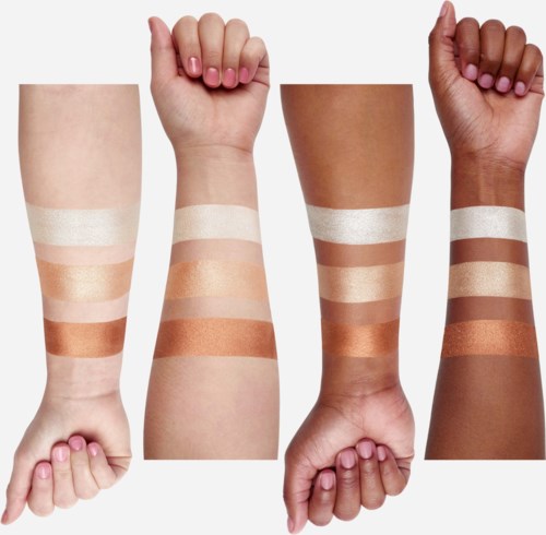 Vier armen met verschillende huidskleuren tonen make-up- of huidverzorgingsstalen op hun onderarmen.