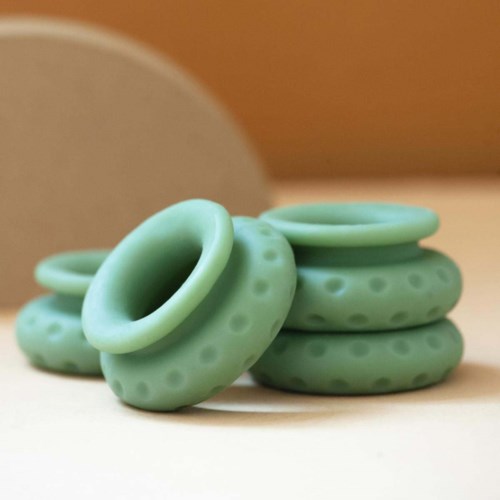Set of six green silicone rings, some stacked and some lying down, with raised dots on them.