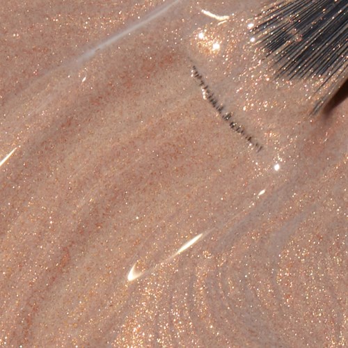 En genomskinlig nagellackflaska med borste ligger på en glittrig, aprikosfärgad yta.