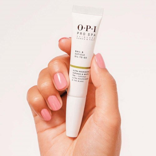En hand håller en liten tub märkt 'O.P.I PRO SPA' för naglar och nagelband, med rosa naglar synliga.