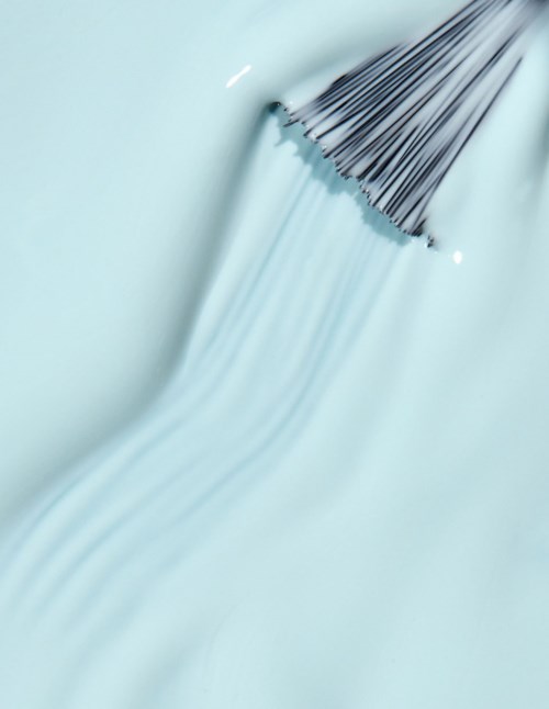 A star-shaped lash brush disperses mascara or makeup on a light blue surface.