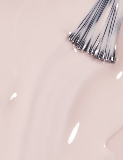 A nail brush with metal bristles near a soft pink background, possibly for painting or cleaning nails.