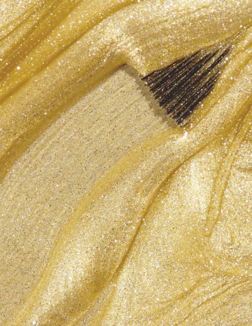 En makeupborste applicerar glittrig, guldfärgad makeup på huden.