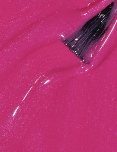 A makeup brush is spreading shiny pink nail polish. The polish shimmers with sparkles.