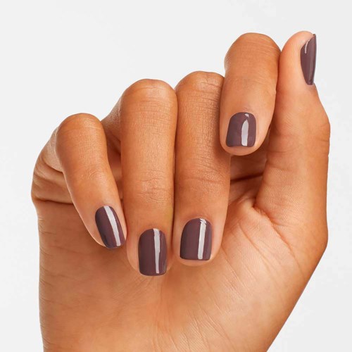 A hand with short nails painted in a dark mauve color, held against a plain background.