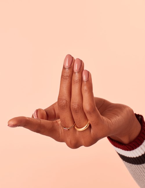 En hand med ringar och målat naglar mot en enkel bakgrund, som visar delikata fingerposer.