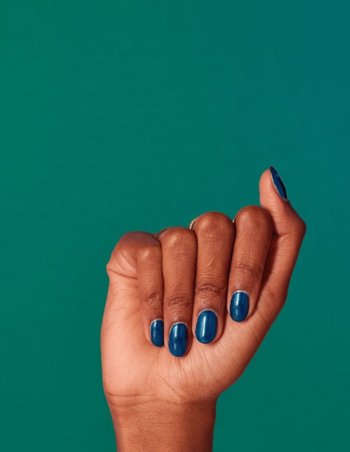 En hand med blå nagellack hålls mot en teal bakgrund.