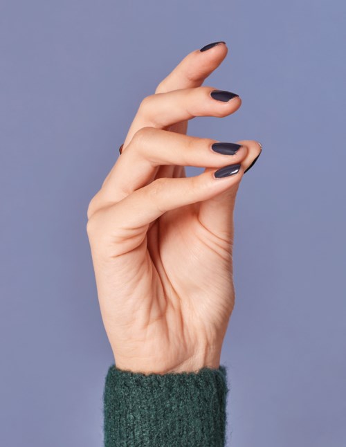 En hand med mörk nagellack är upphöjd mot en enkel blå bakgrund.