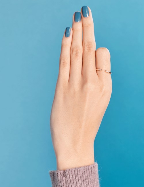 En hand med blå nagellack och en ring, vinklad mot en blå bakgrund.