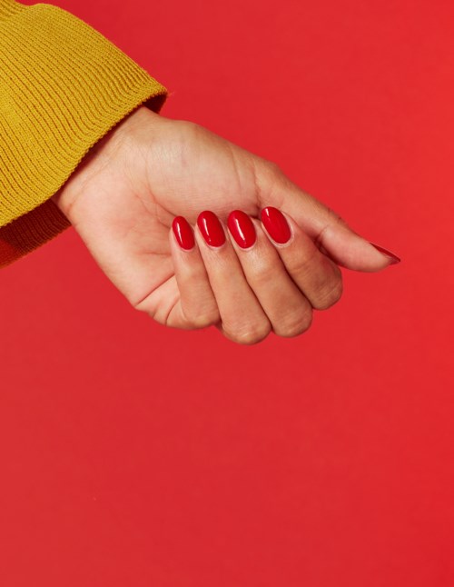 En hand med röda nagellack pekar åt höger mot en röd bakgrund, med en gul ärm.
