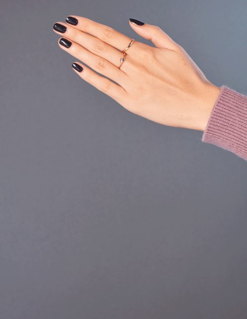En hand med ringar och svart nagellack sträcks ut mot en enkel grå bakgrund.