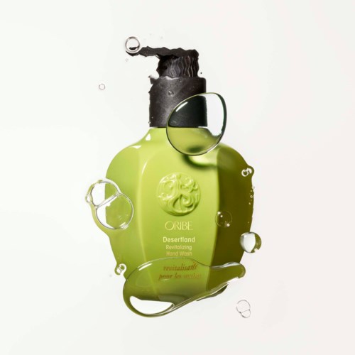 A green hand wash bottle with black cap, surrounded by water bubbles, on a white background.