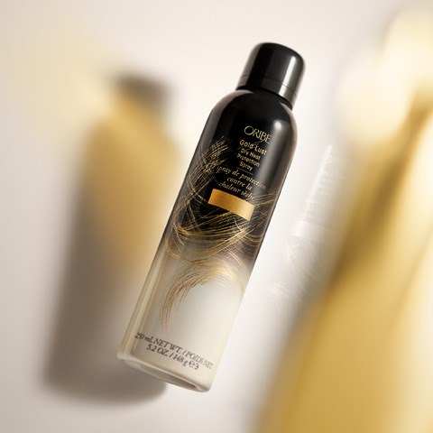 Eine schwarze und goldene Flasche mit Oribe Trockenkunstspray, mit einer seidigen Spiraldrehung. Schatten und Licht betonen die Flasche.