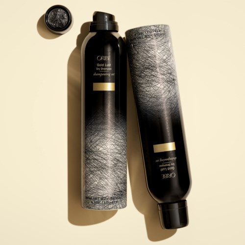 To svarte flasker av Oribe sjampon ligger på en beige overflate, med en liten kork og tilhørende etikett.