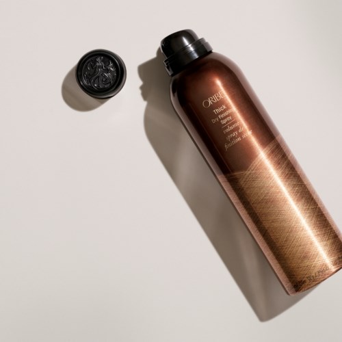 Eine braune Flasche Oribe Haarspray auf weißer Oberfläche mit einem schwarzen Deckel in der Nähe.