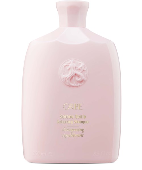 Een lichtroze shampoo fles met een reliëf embleem en gouden tekst, gemarkeerd als Oribe Serene Scalp Balancing Shampoo.