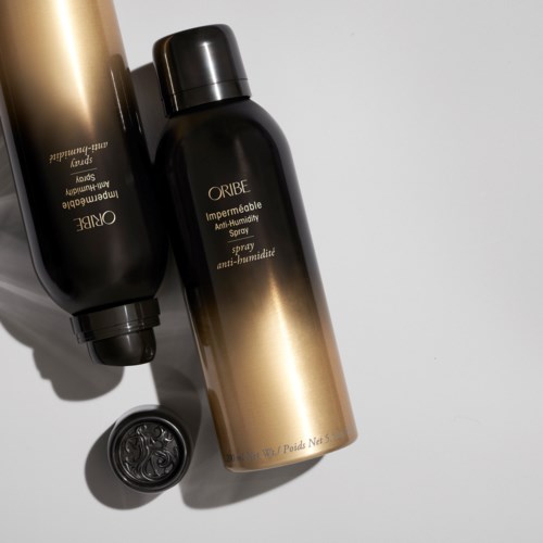 Zwei schwarz-goldene Sprühflaschen mit der Aufschrift ORIBE Anti-Humidity, mit schwarzem Deckel und kleiner Dose daneben.