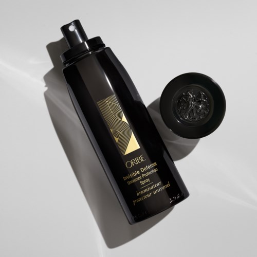 Eine schwarze Sprühflasche mit goldener Beschriftung neben einem runden Deckel auf weißer Oberfläche.
