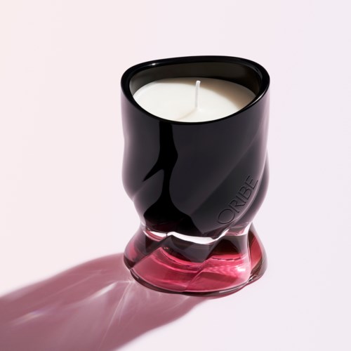 Ein schwarzer und pinker Kerzenhalter mit weißer Kerze, die einen Schatten auf eine helle Oberfläche wirft.