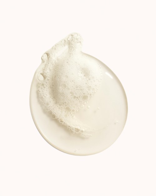 Eine klare, runde Milch-Tropfen mit Blasen oben auf weißem Hintergrund.