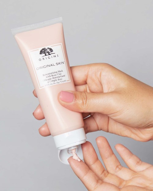 Een hand houdt een roze tube met Origins huidverzorgingscrème en knijpt er wat uit op de vinger.