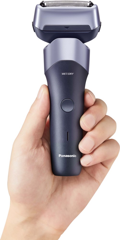 A hand holding a gray and black electric shaver with a large shaving head. The shaver has a power button and brand name Panasonic.