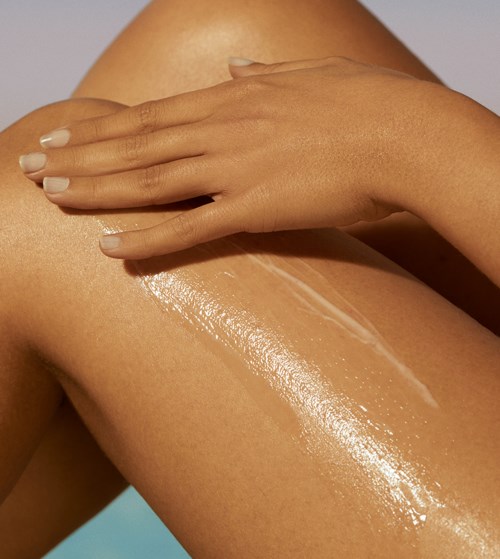 Eine Person trägt Lotion oder Öl auf ihr Bein auf, das glänzend und gut gepflegt aussieht.