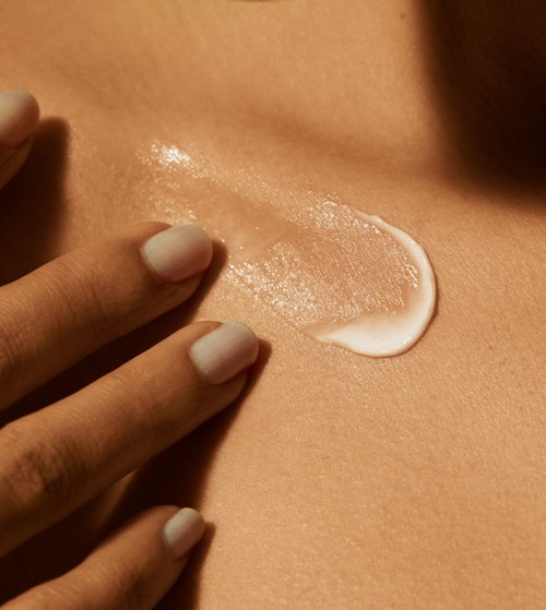 Eine Person trägt weiße Creme mit den Fingern auf die Haut auf, mit glatter und glänzender Oberfläche.