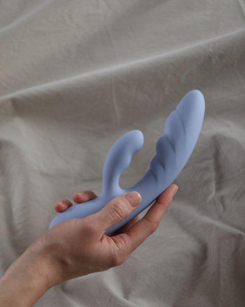 Eine Hand hält ein blaues, gebogenes, geripptes Objekt, das wie ein Spielzeug oder Werkzeug aussieht, vor einem neutralen Hintergrund.
