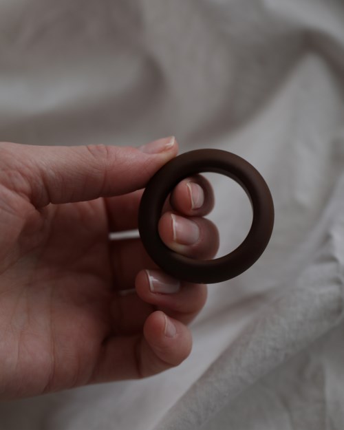 Eine Hand hält einen dunklen runden Gegenstand, möglicherweise einen Ring, vor einem weißen Stoffhintergrund.