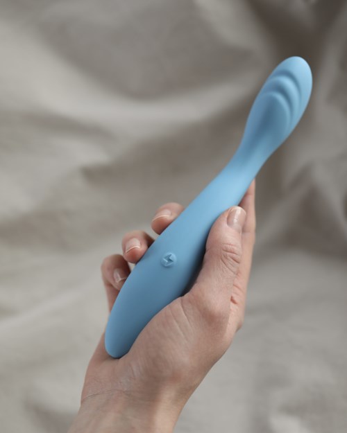 Eine Hand hält ein blaues, gebogenes, glattes Objekt, das wie ein persönliches Pflegegerät aussieht.