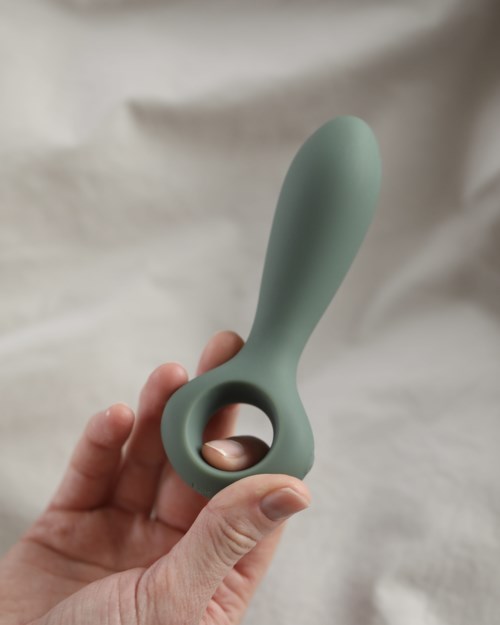 Ein grünes Silikon-Gerät mit einer Schlaufe und einem langen Griff, gehalten in jemandes Hand.
