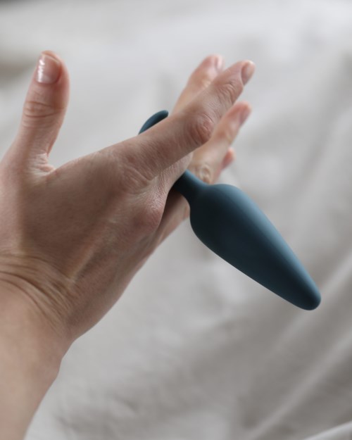 Eine Hand hält ein dunkelblaues, gebogenes Objekt über einem hellen Hintergrund.