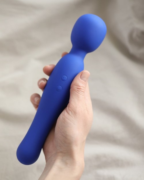 Eine Hand hält eine blaue Massagevibrator mit runder Spitze und Knöpfen am Griff.