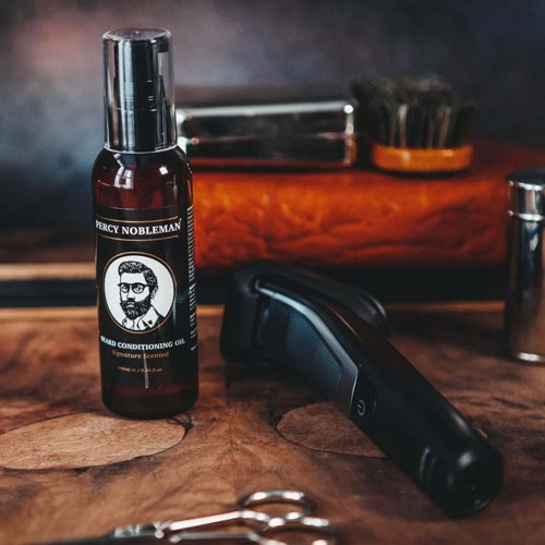 A grooming kit with a hair clipper, brush, and oil bottle on a wooden surface.