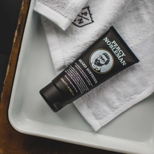 A black tube labeled 'Beard Softener' lies on a white towel on a tray.