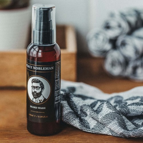 Eine Flasche mit 'Beard Wash' auf einer Holzoberfläche, mit einem Tuch in der Nähe, in einer gemütlichen Umgebung.